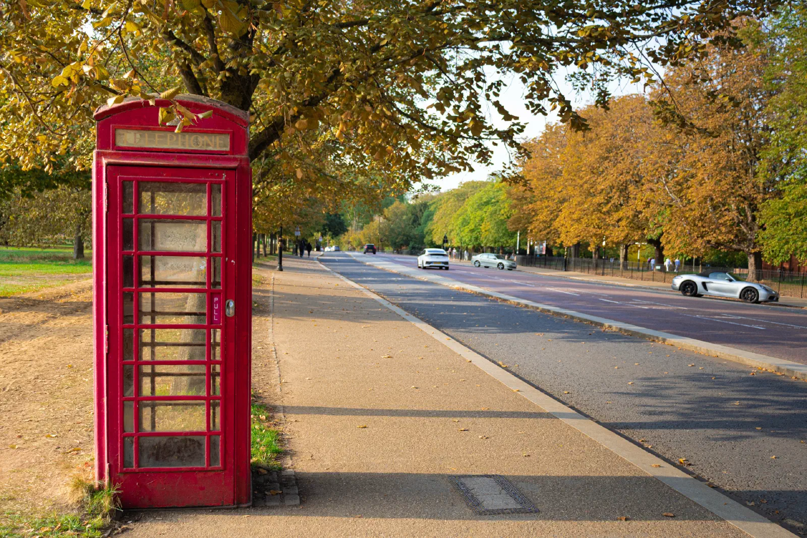 Cabine telefônica vermelha em uma avenida arborizada de Londres, no outono